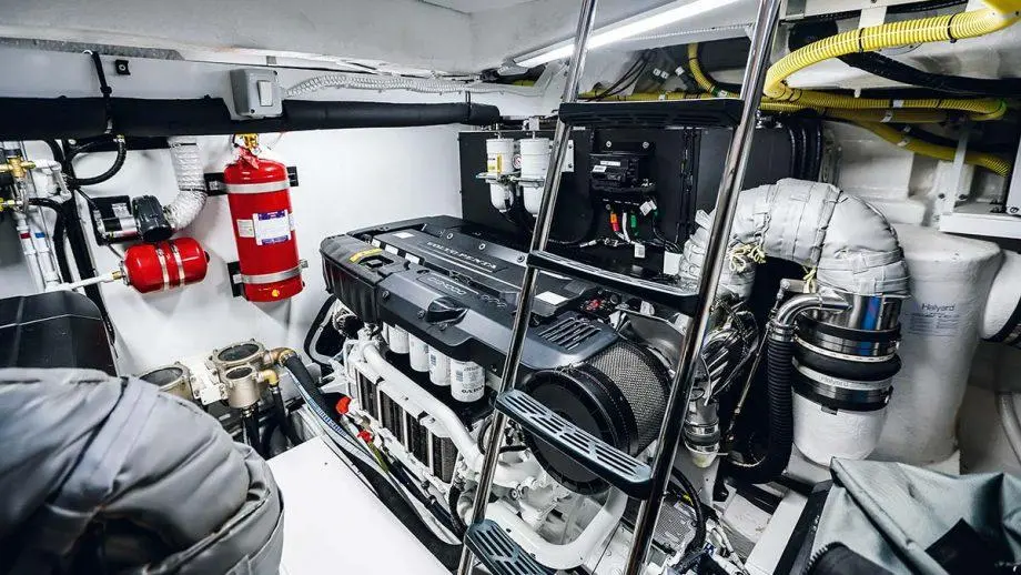 Engine room with a large marine engine, fire extinguisher, and visible pipes, surrounded by access ladders and machinery.